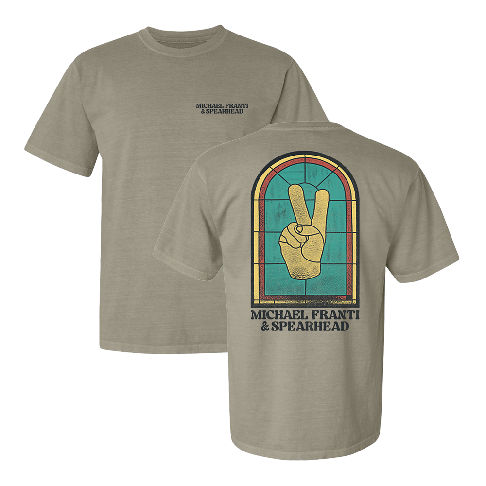 Tan t-shirt with a peace sign design on the back and band name on the front.