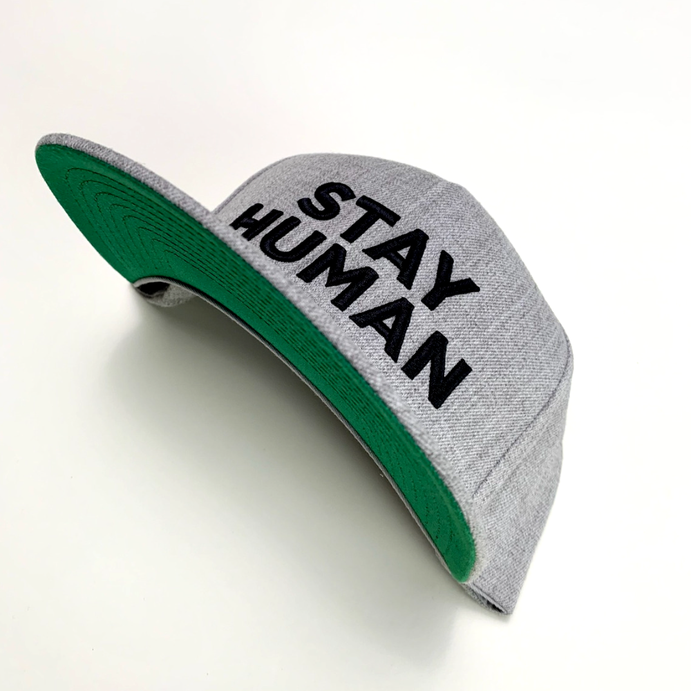 Gray baseball cap with a green brim and ’STAY HUMAN’ text on the front.